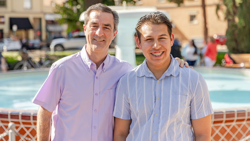 Outdoor photo of two people smiling, standing in front of fountain